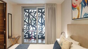A hotel room with a large bed, a sliding glass door leading to an outdoor area with a table and chairs, and a painting on the wall. - Modern Studio w Rooftop Pool Near Beach & Dining (Playa del Carmen)