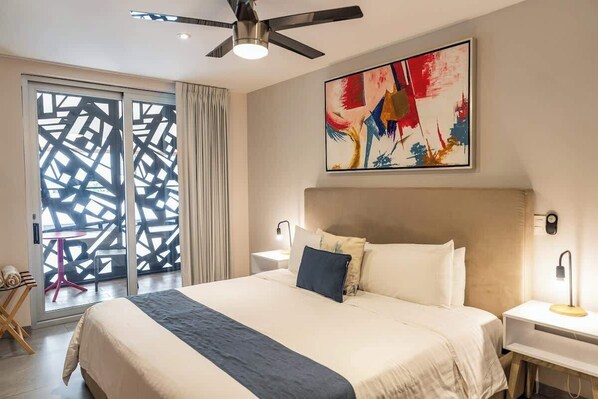 A modern hotel room with a large bed, a ceiling fan, a painting, and a view through a patterned door. - Modern Studio w Rooftop Pool Near Beach & Dining (Playa del Carmen)