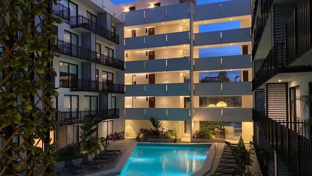 Un hotel de varios pisos con piscina, balcones y mobiliario exterior.