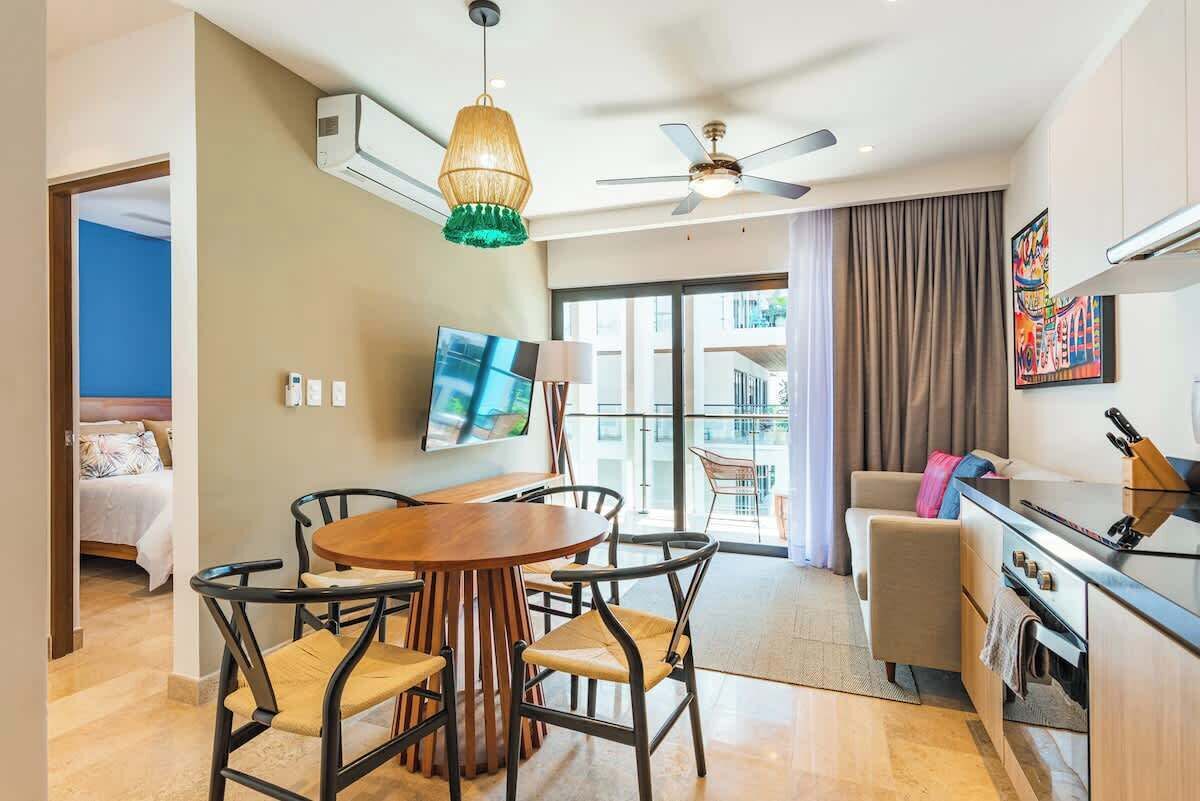 A modern hotel room with a dining area, a sofa, a TV, and a ceiling fan.