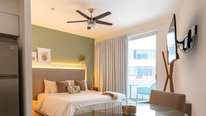 Ein modernes Hotelzimmer mit Bett, einem Glastisch, Stühlen, einem Deckenventilator und einem großen Fenster mit Vorhängen.