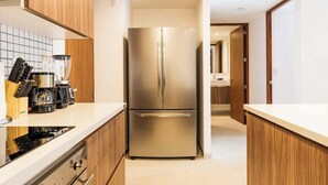 A modern kitchen with a stainless steel refrigerator, wooden cabinets, and a white countertop. - 1BR Condo w Rooftop Pool Steps from Beach & 5th Ave (Playa del Carmen)