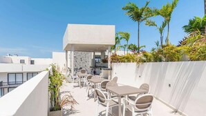 A rooftop terrace with outdoor seating, a covered area, and surrounding vegetation. - 1BR Condo w Rooftop Pool Steps from Beach & 5th Ave (Playa del Carmen)