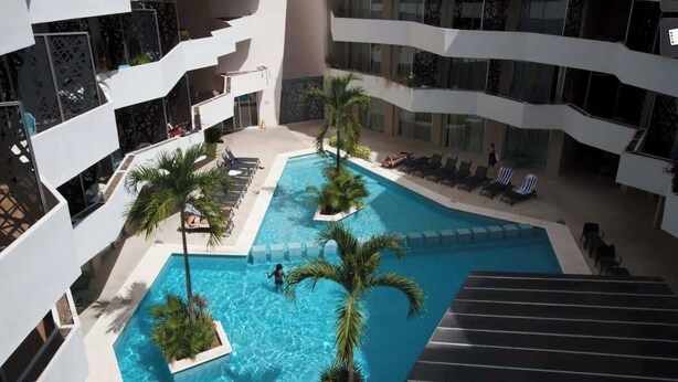 A multi-level indoor pool with clear blue water, surrounded by palm trees and lounge chairs. - Rooftop Pool & Gym Near 5th Avenue Activities (Playa del Carmen)