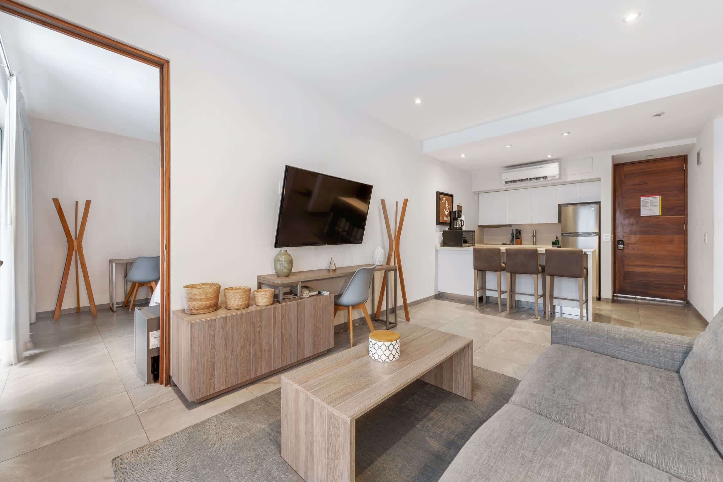 Un salon moderne avec un canapé, une table basse et un téléviseur. Il y a également un coin cuisine avec une table à manger et des chaises.