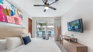 A modern hotel room with a large bed, a ceiling fan, a TV, and a view of the pool area. - Rooftop Pool & Gym Near 5th Avenue Activities (Playa del Carmen)