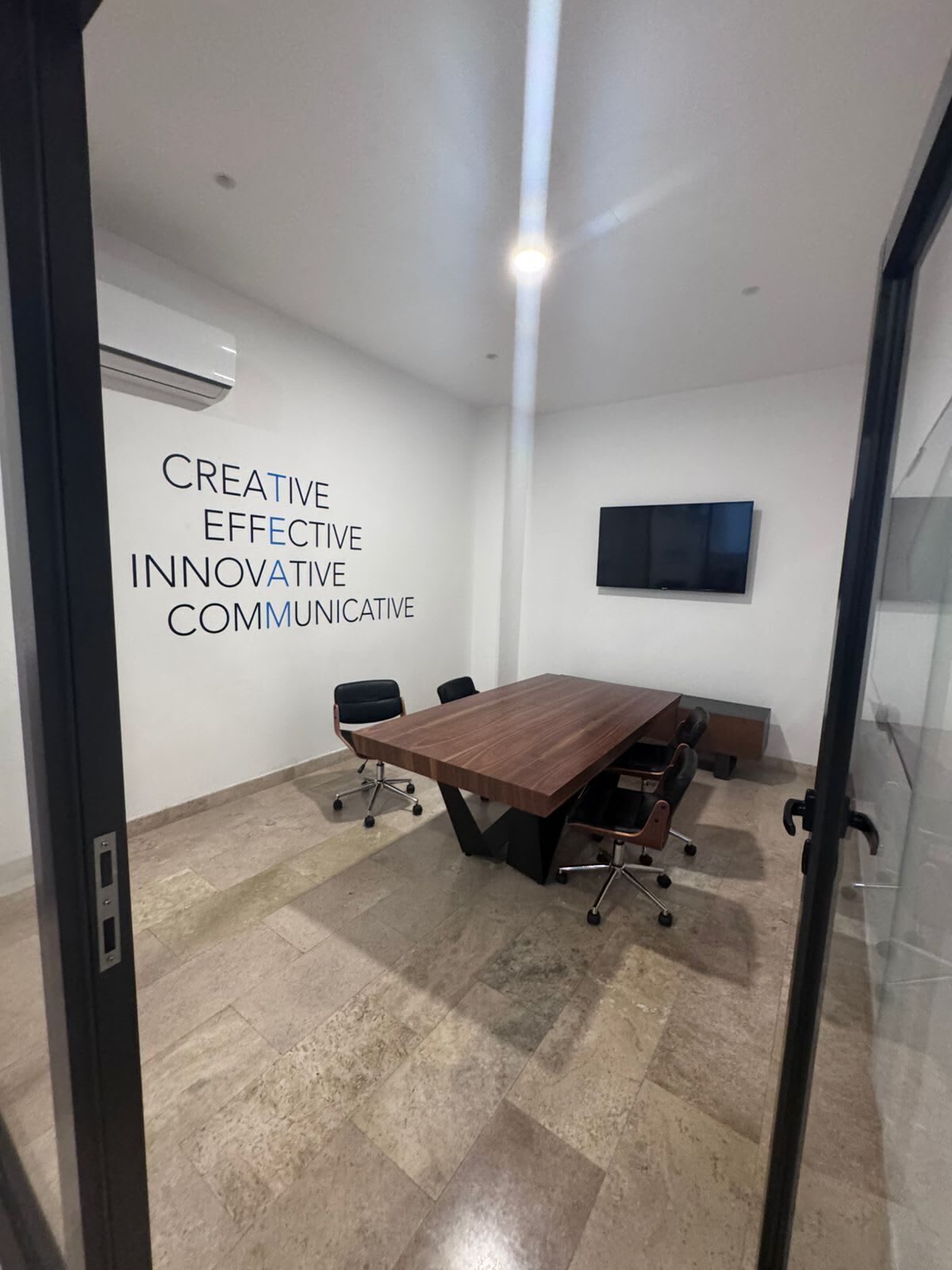 A conference room with a large wooden table, black chairs, a flat-screen TV on the wall, and a motivational quote on the wall.