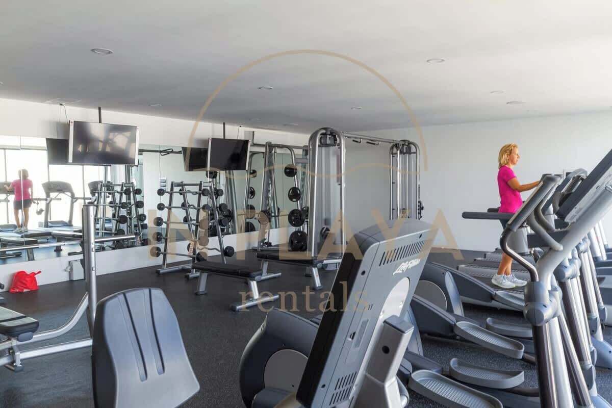 A gym with treadmills, weight machines, and a television screen.