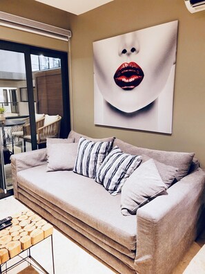 A living room with a sofa, pillows, a coffee table with wood logs, and a large wall art piece. - Stylish 1BR Beachside Retreat (Playa del Carmen)