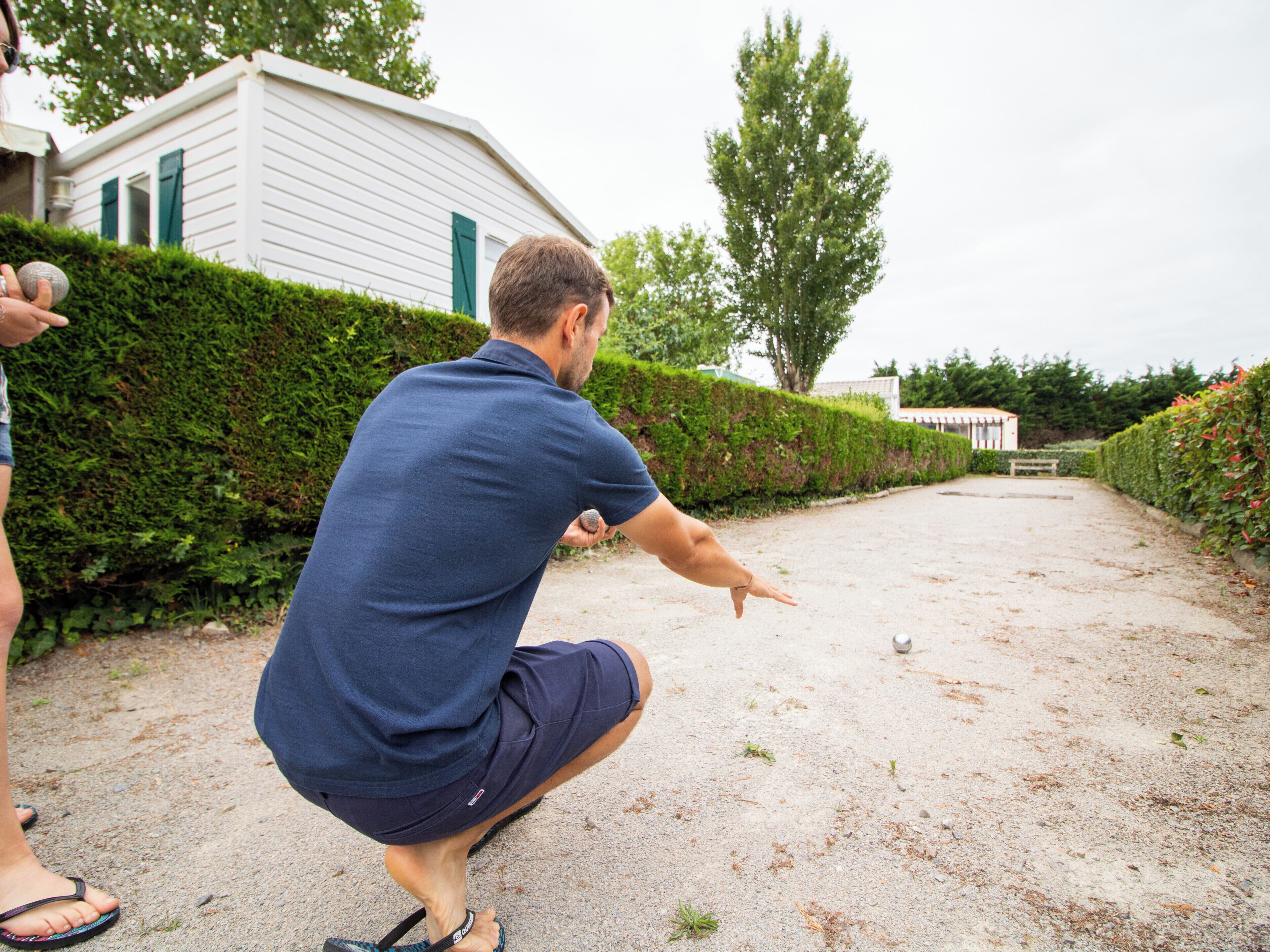 Ein Mann in blauem Hemd und Shorts kniet auf einem Schotterweg und zielt auf einen Golfball.