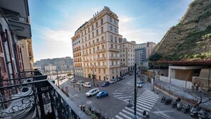 En byggnad med flera våningar i en klassisk arkitektonisk stil, en gata med bilar och ett övergångsställe, samt en utsikt över det omgivande stadsområdet.