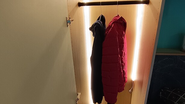 Een kleine, afgesloten kast met een houten deur, een kledingstang en een plank.