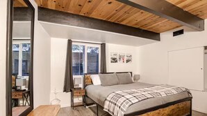 Une chambre à coucher avec un lit en bois, un banc, un bureau et une fenêtre avec des rideaux.