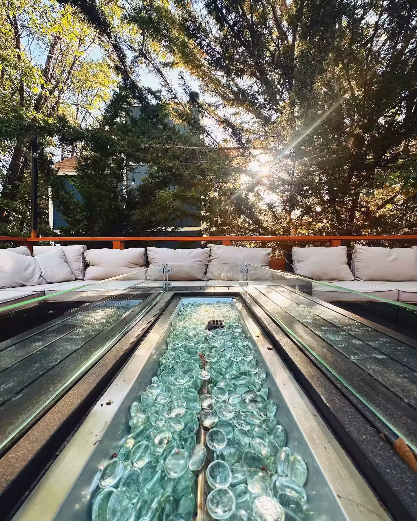 A pool table with scattered glass bottles, surrounded by outdoor seating with cushions.