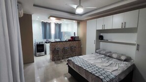 A modern bedroom with a large bed, a built-in wardrobe, and a kitchenette area. - Complete Studio 3 (Rio das Ostras)