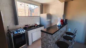A compact kitchen with a gas stove, a refrigerator, a sink, and a small bar area with two stools. - Complete Studio 3 (Rio das Ostras)