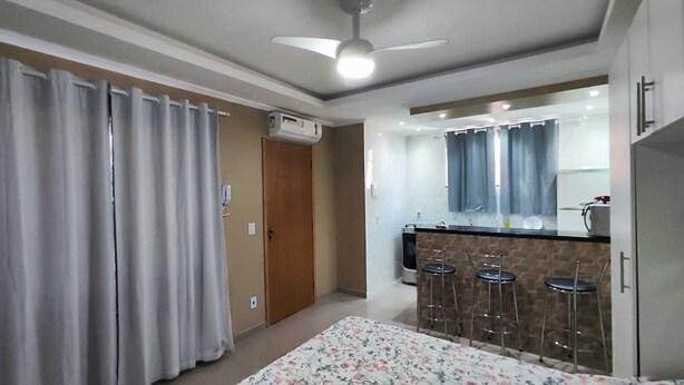 A compact room with a kitchenette, a ceiling fan, and a door leading to another room. - Complete Studio 3 (Rio das Ostras)