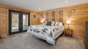 Een slaapkamer met een bed, twee nachtkastjes met lampen, een houten wandpaneel en een deur naar buiten.