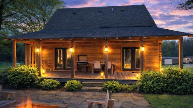 Een houten chalet met een overdekte veranda, vuurkorf van natuursteen en buitenmeubilair.