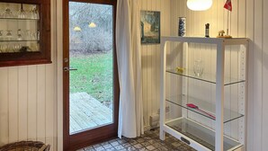 Una habitación con una puerta de madera, un aparador de vidrio con estantes y una mesita con una lámpara.