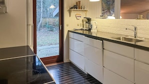 Una cocina moderna con armarios blancos, encimera negra y pileta de acero inoxidable. Hay una cafetera y un hervidor en la encimera, y una puerta que da a un patio trasero.