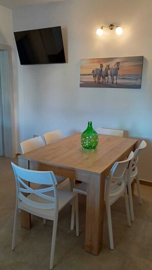 A dining area with a wooden table, white chairs, a green bottle, a painting of horses, and a mounted TV. - Villa Piro: detached villa with garden, veranda and BBQ, Litorale di Manduria (Urmo)
