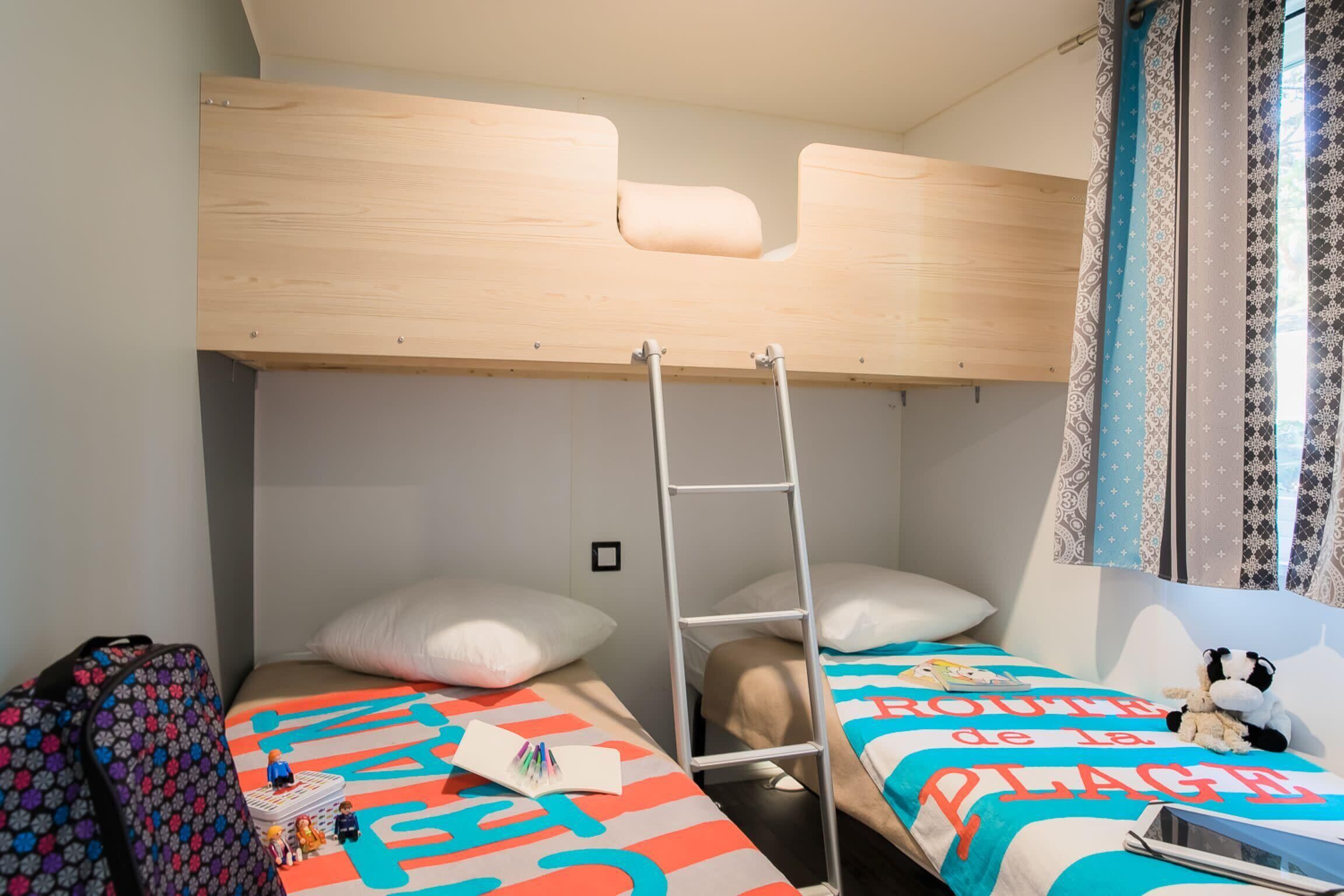 Een slaapkamer met een stapelbed, een ladder, een koffer en een bed met een kleurrijk dekbed.