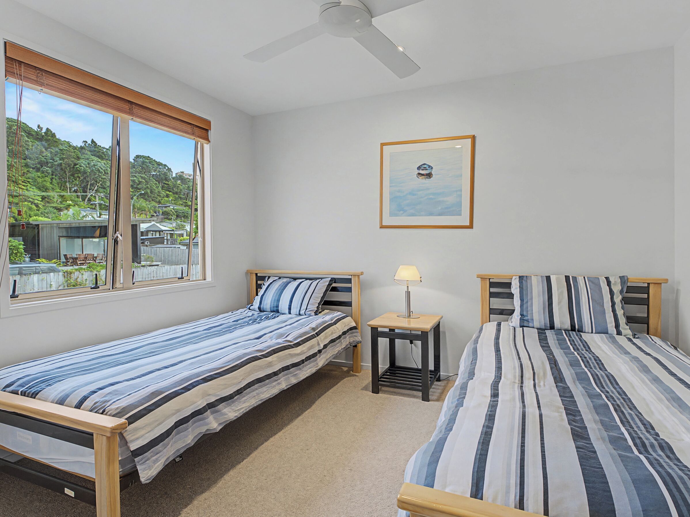 A bedroom with two single beds, a ceiling fan, a small table with a lamp, and a framed picture on the wall.