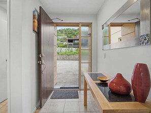 A hallway with a wooden door leading to a balcony, a small table with a bowl and a vase, and a mirror on the wall.