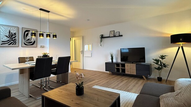 A modern living room with a dining area, a flat-screen TV, and a floor lamp. - Old Town Residence Warendorf (Warendorf)