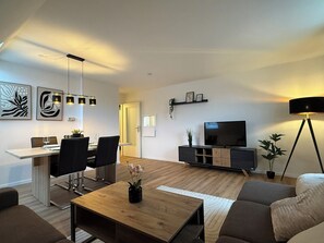 Ein modernes Wohnzimmer mit Essbereich, einem Flachbildfernseher und einer Stehlampe.