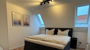 A bedroom with a bed, two windows, a chair, and two wall-mounted pictures. - Old Town Residence Warendorf (Warendorf)