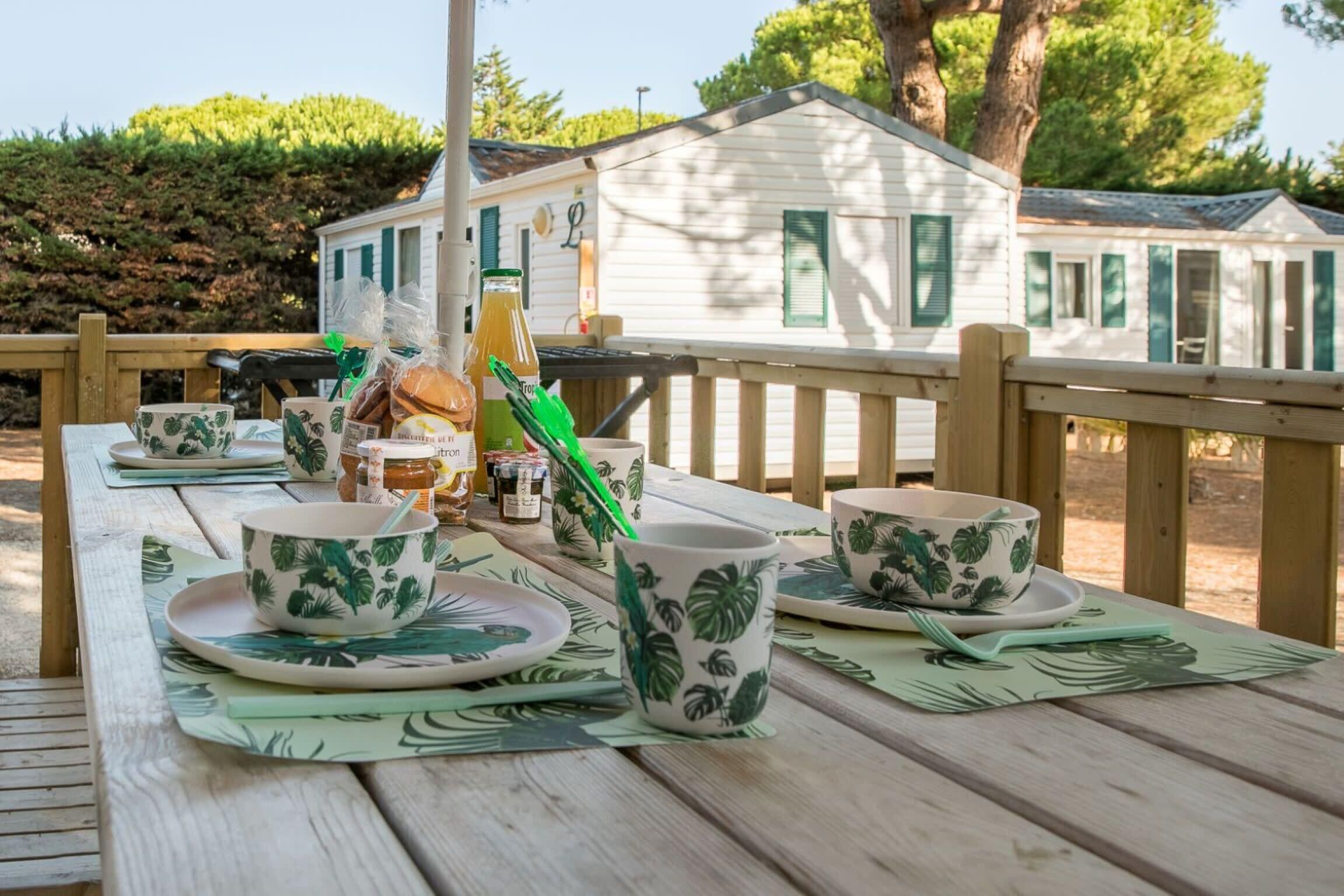 Eine Holzterrasse mit Picknick-Ausrüstung, tropisch gestaltetem Geschirr und einer Saftflasche.