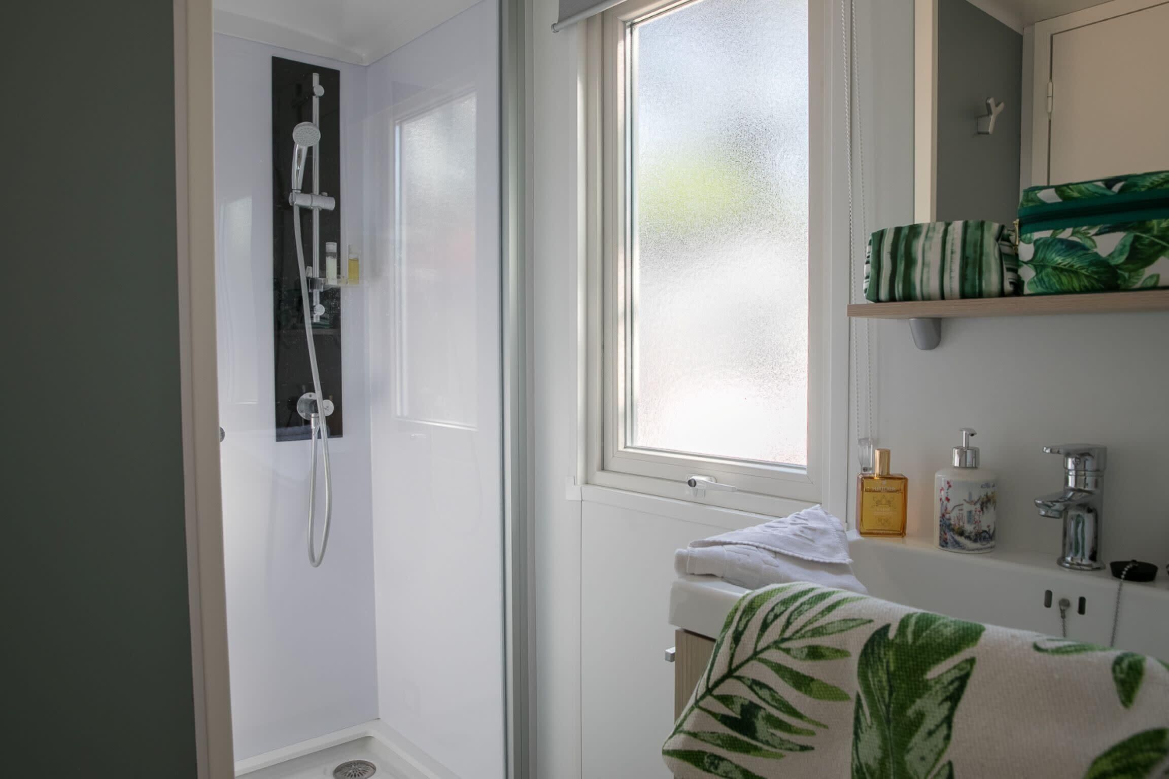 Ein Badezimmer mit Dusche, Fenster, Waschbecken und Handtuchhalter.