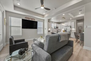 Ein modernes Wohnzimmer mit grauem Sofa, einem Glastisch und einem Deckenventilator.