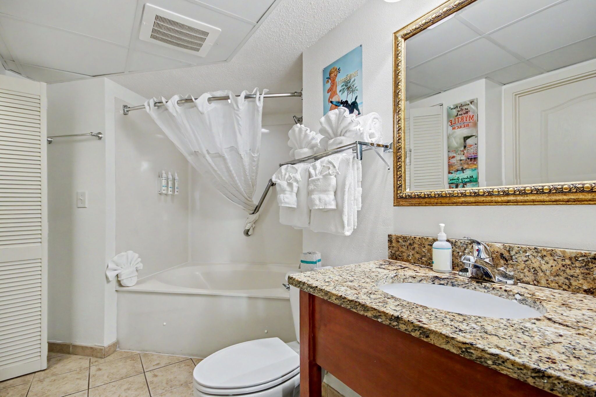 A bathroom with a bathtub, toilet, sink, and a mirror with a decorative frame.