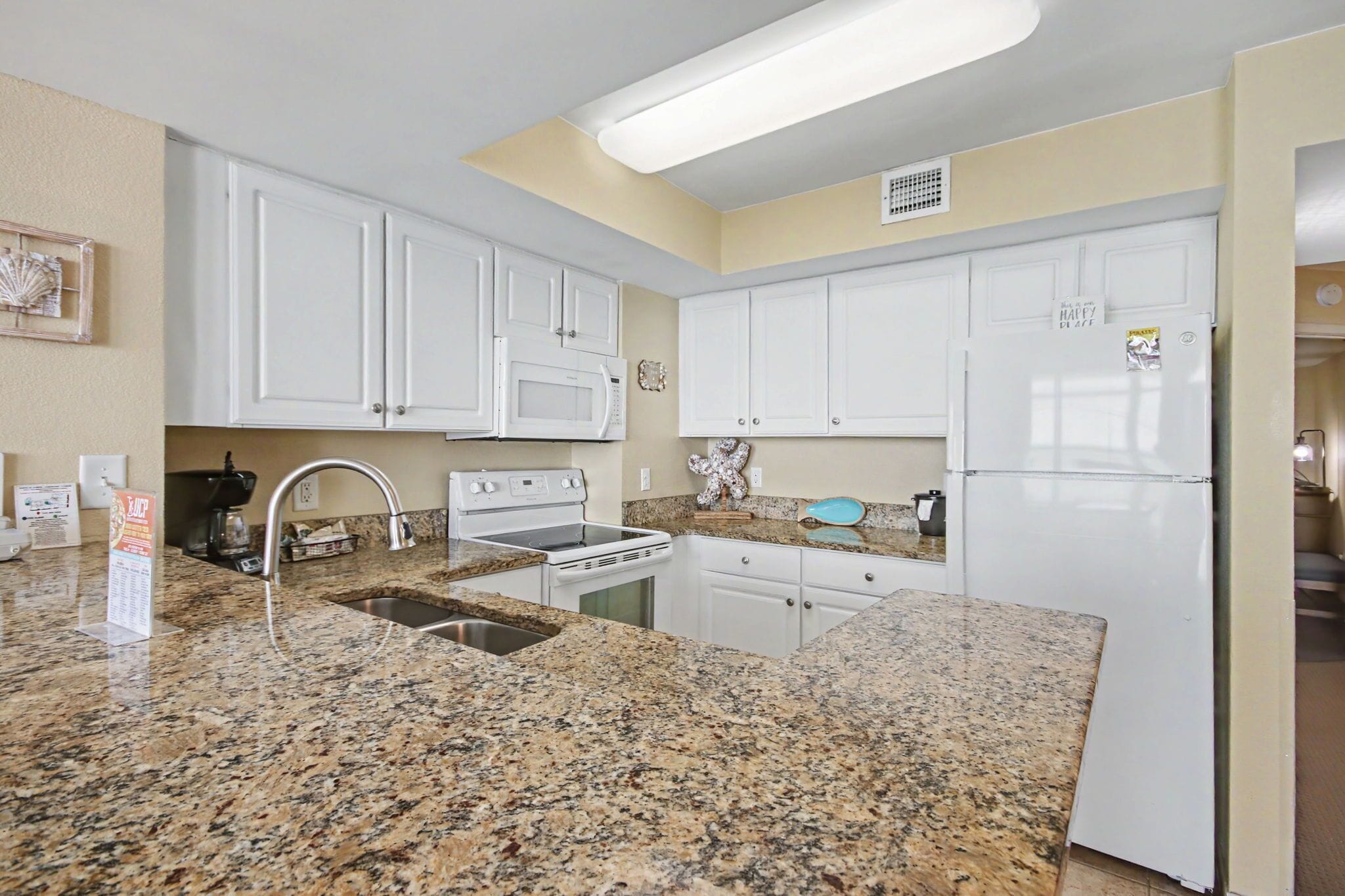A kitchen with white cabinets, granite countertops, a microwave, stove, sink, and a refrigerator.