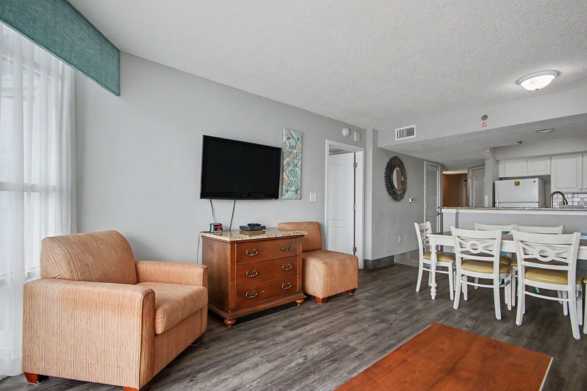 A living room with a sofa, a wooden cabinet, a flat-screen TV, and a dining area with chairs.