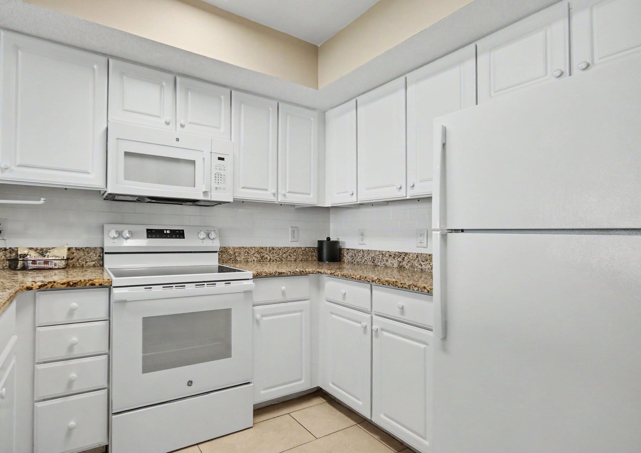 A kitchen with white cabinets, a microwave, stove, and refrigerator.