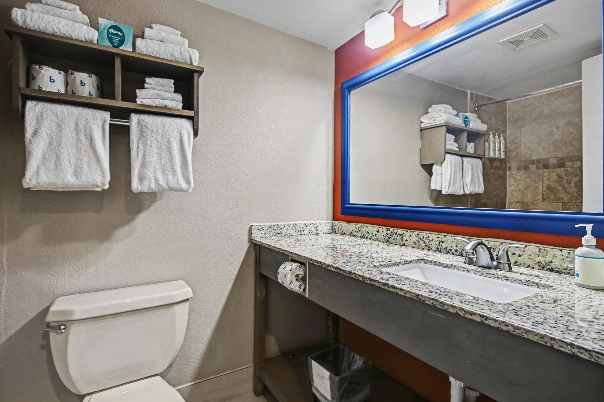 A bathroom with a toilet, a sink, a mirror, and shelves with towels.