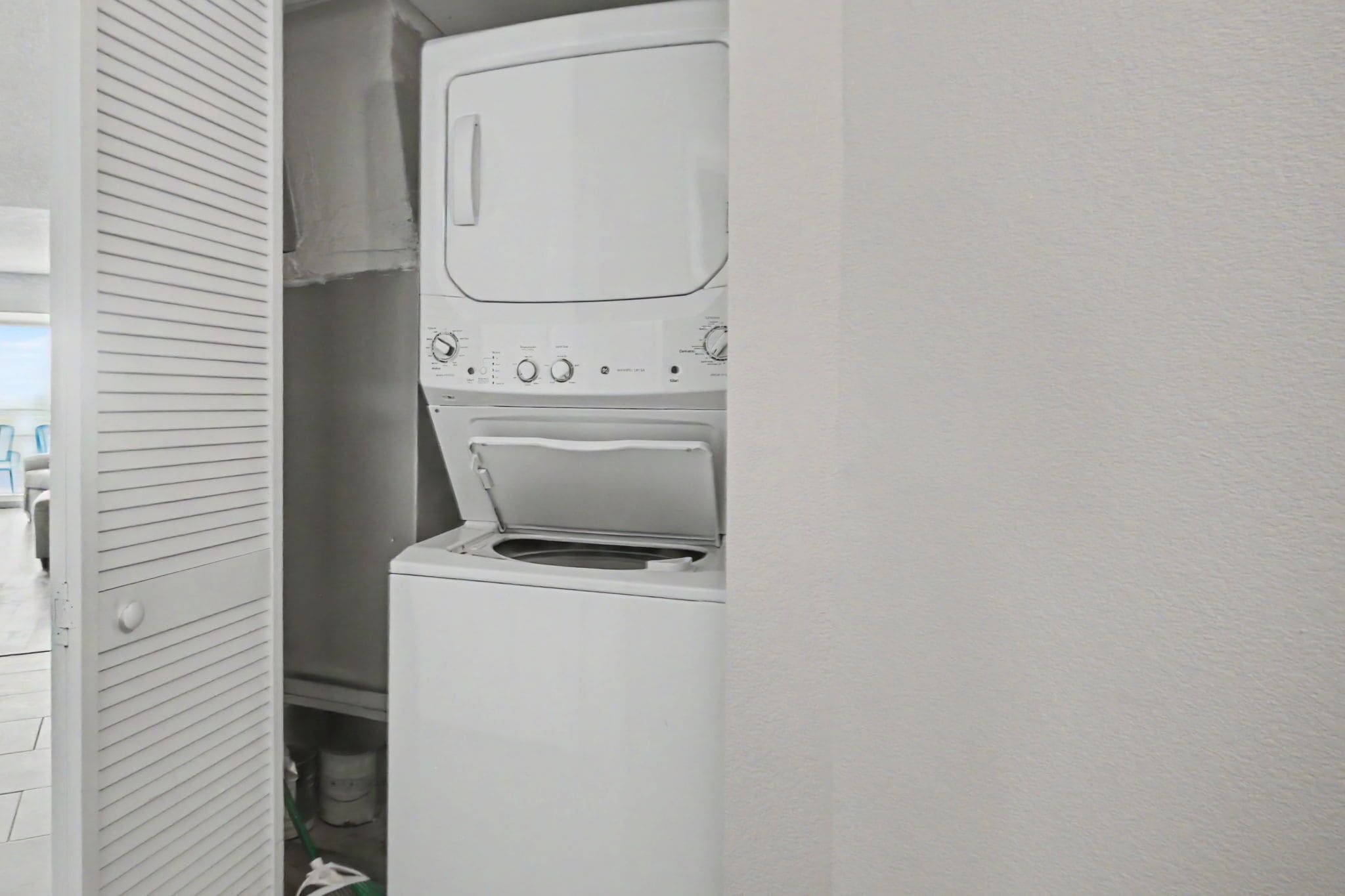 Un espace buanderie compact comprenant un lave-linge et un sèche-linge, une porte aux lignes horizontales et un sol visible.