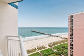 A balcony with a view of a beach, a pier extending into the ocean, and a building with multiple balconies. - Carolinian Beach Resort (Myrtle Beach)