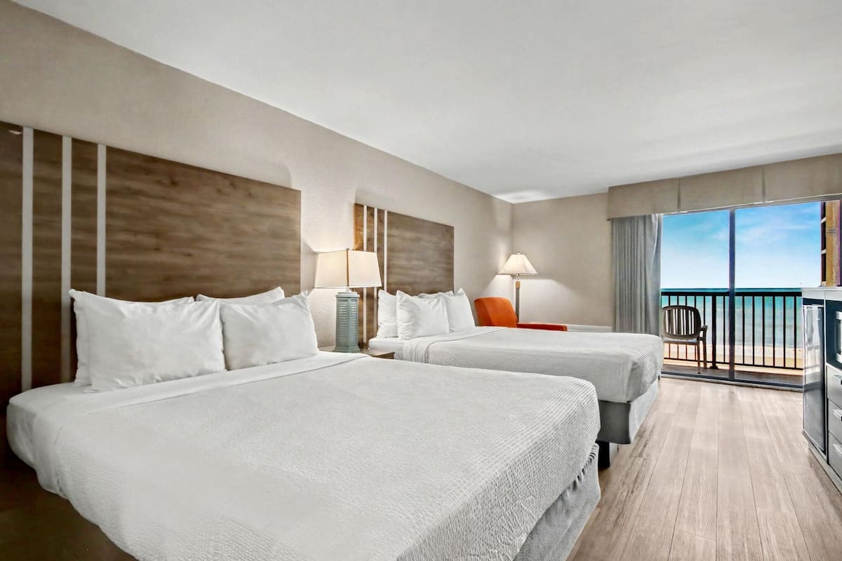 Una habitación de hotel con dos camas, un balcón con vistas y un escritorio con lámpara.