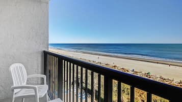 A balcony with a view of the beach, a white chair, and a table.