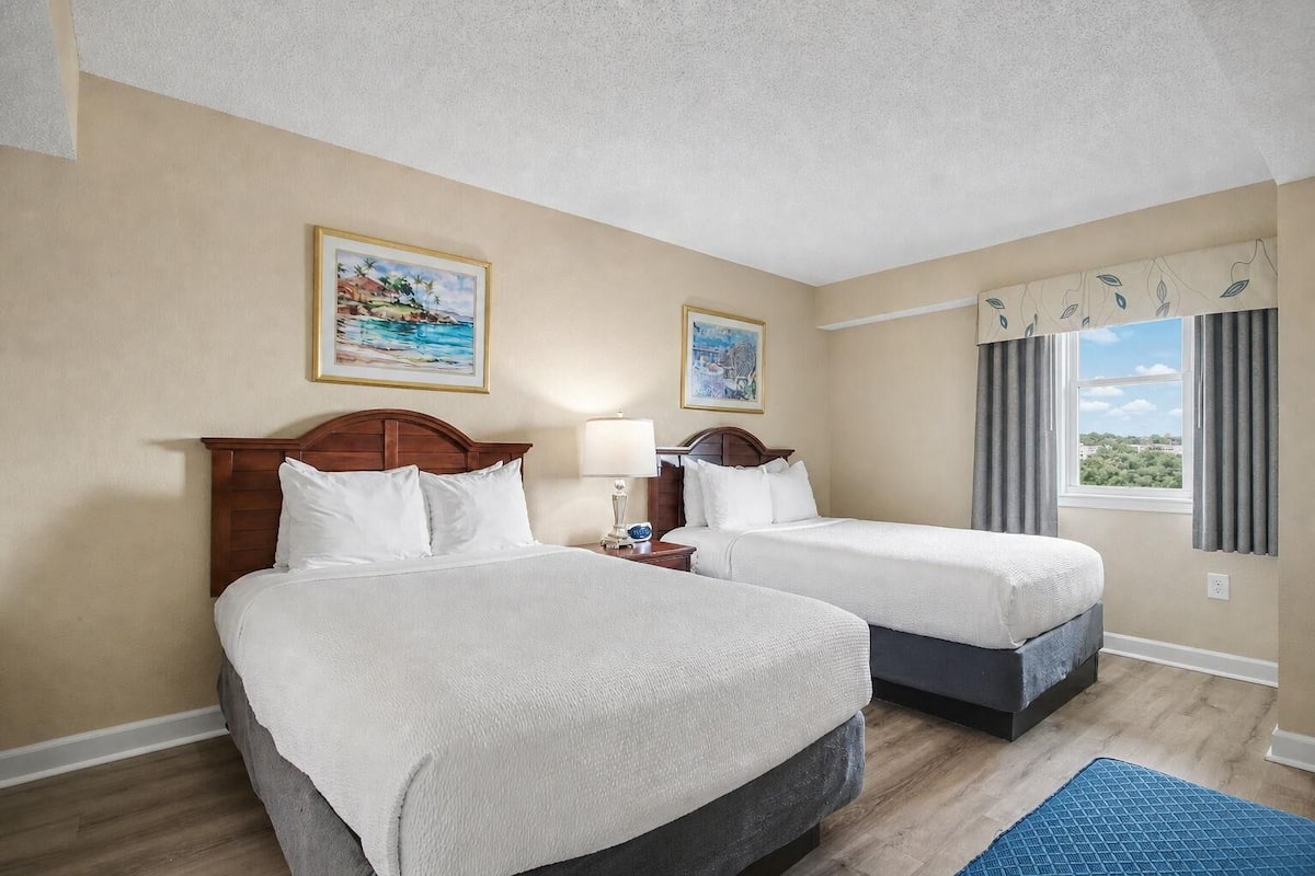 Una habitación de hotel con dos camas, una ventana con cortinas y dos cuadros en la pared.