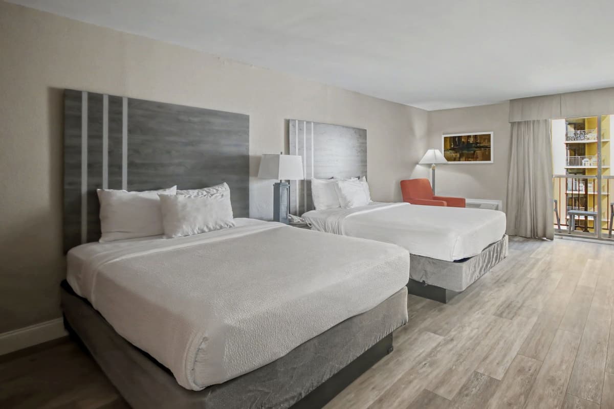 Habitación de hotel con dos camas, una silla roja, una lámpara y vistas a un balcón con barandilla.
