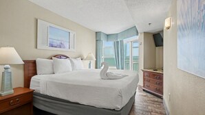 Une chambre d’hôtel avec un lit, des tables de chevet, une commode, un tableau et une vue sur l’extérieur.