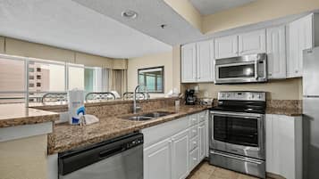 A modern kitchen with white cabinets, stainless steel appliances, a dishwasher, and a large window offering a view of the outside.