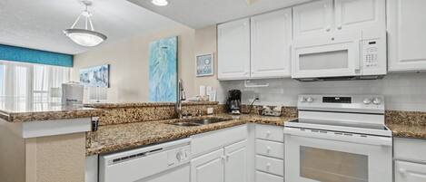 A modern kitchen with white cabinets, granite countertops, a built-in microwave, and a dishwasher.