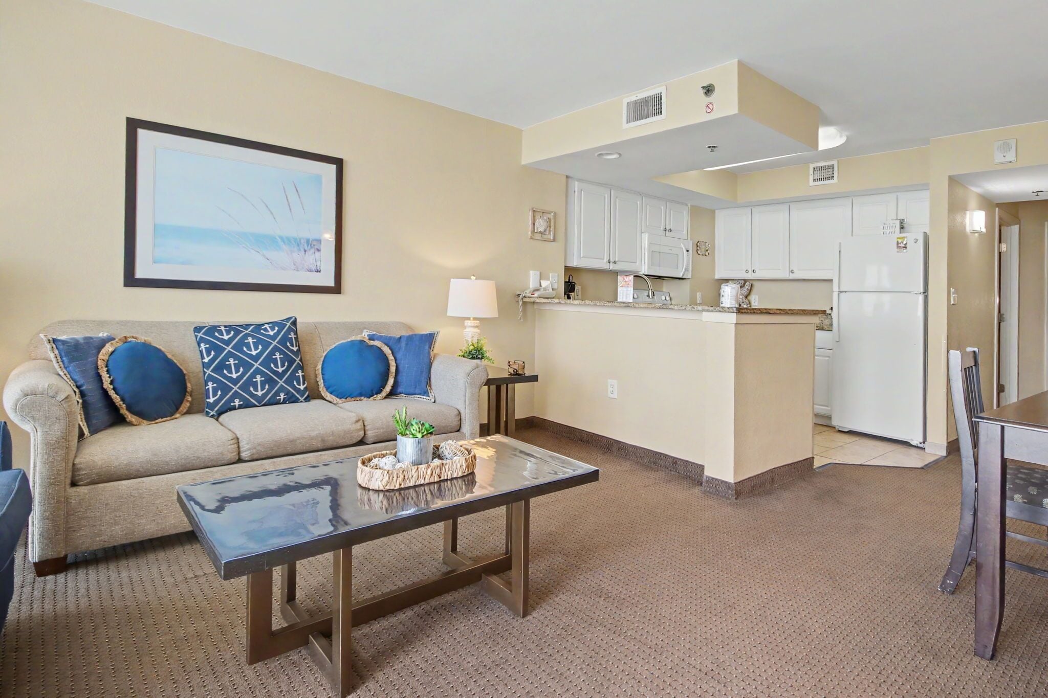A living room with a sofa, coffee table, and a kitchen area with cabinets and appliances.